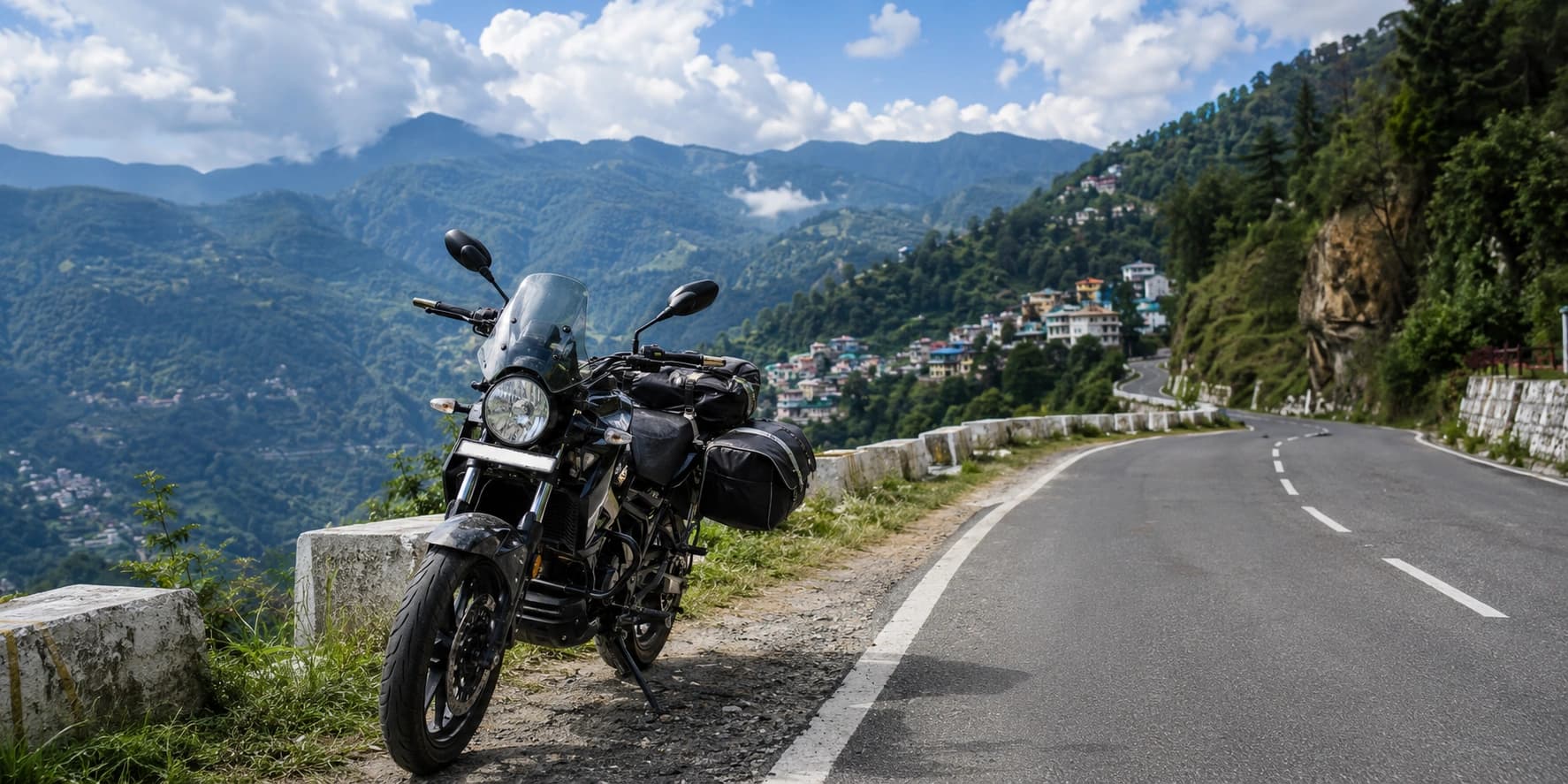 A black touring motorcycle with luggage parked beside a winding mountain road overlooking green hills and a hill station in India.
